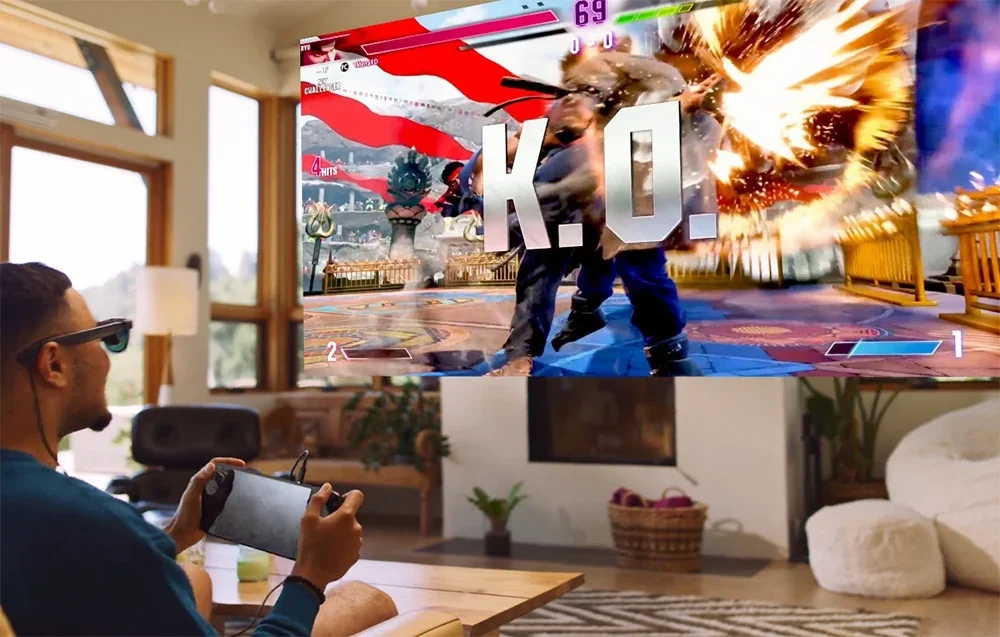 Vīrietis ar XR brillēm spēlē cīņas spēli uz portatīvās konsoles, kas redzama lielajā ekrānā