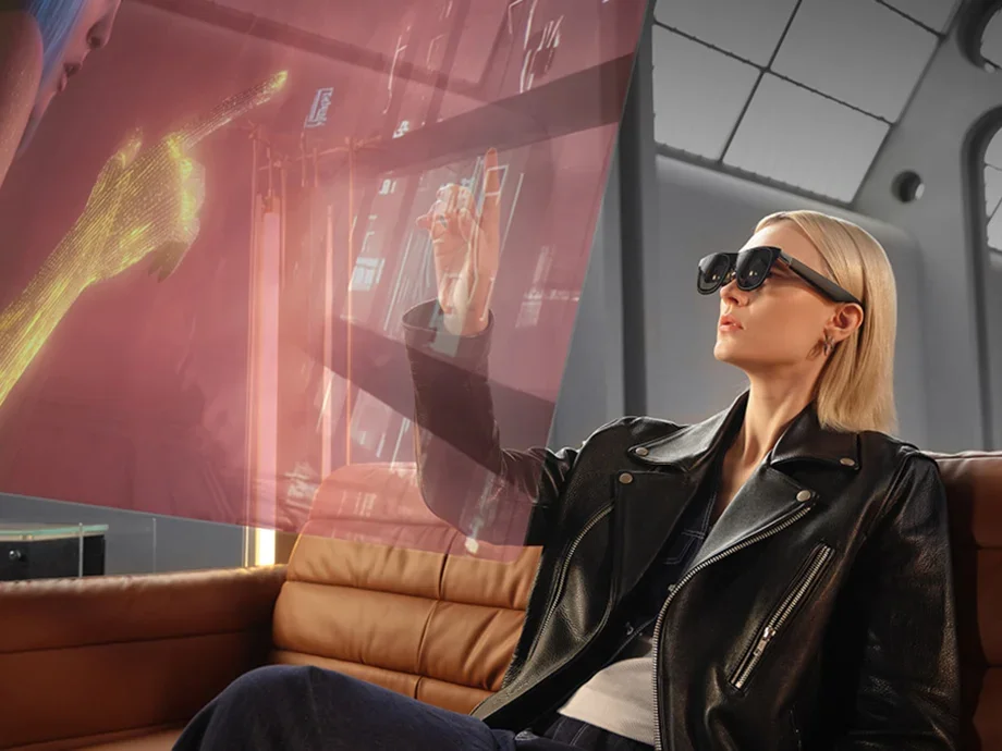 A woman wearing AR glasses sitting on a couch and interacting with a translucent holographic interface.