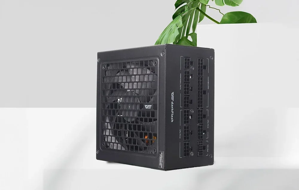 Melns DarkFlash barošanas bloks uz balta galda virsmas ar zaļu augu fonā